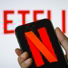 a person holds a smartphone in vertical orientation displaying the red N logo of Netflix